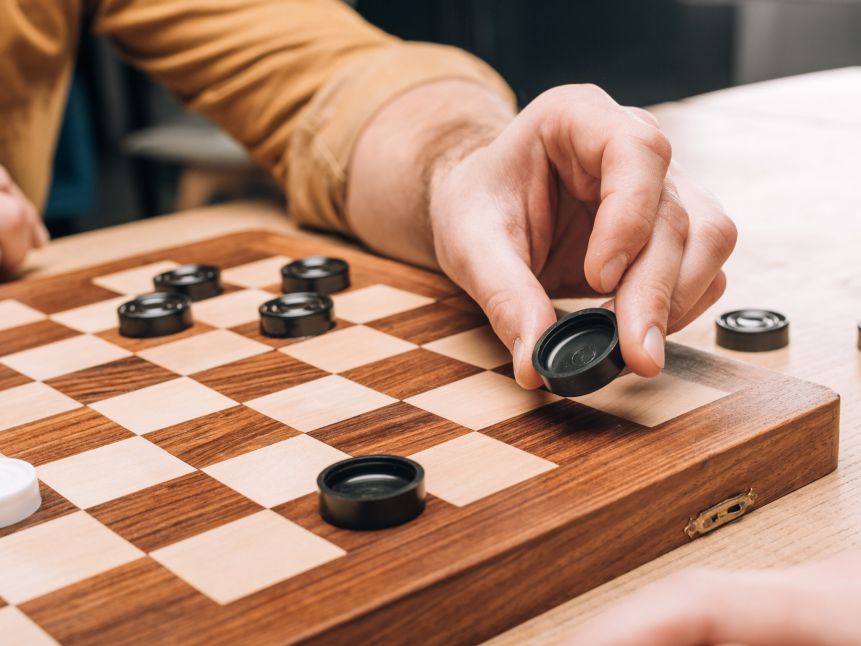 Selective focus of man holding black checker on wooden checkerboard